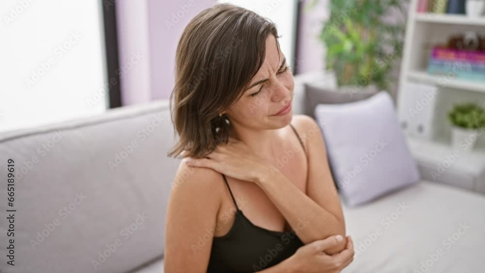 Young beautiful hispanic woman sitting on sofa suffering for cervical pain at home