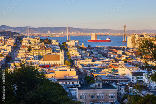 Sunset glow over residential San Francisco city with tanker in bay under Oakland Bay Bridge