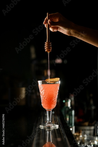 фотографія Woman bartender's hand holding wooden spoon and adding honey to old-fashioned dr