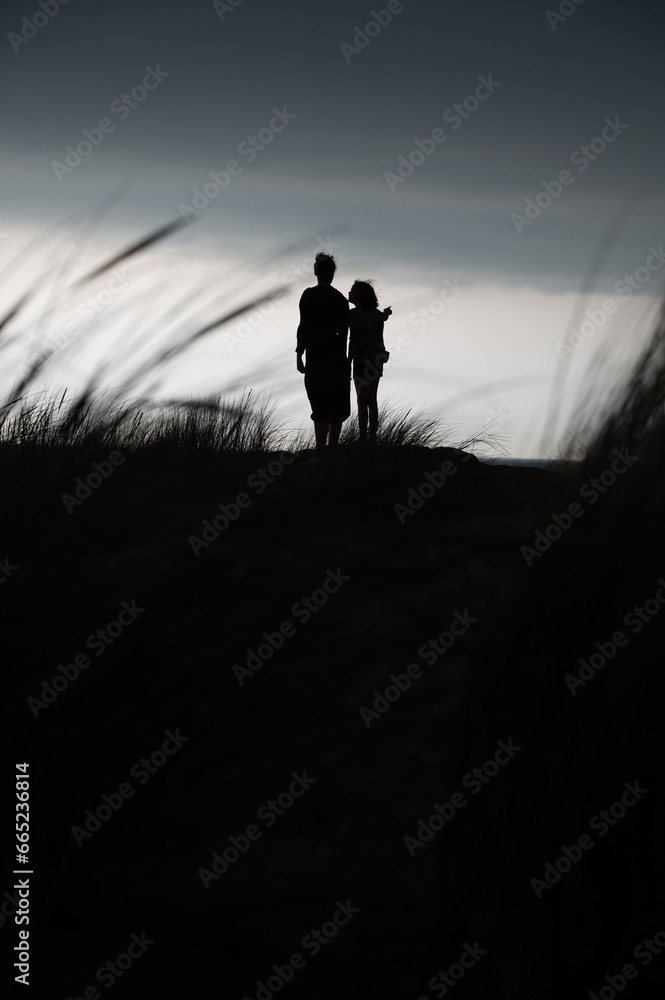 silhouette of two person standing on a rock at the sea