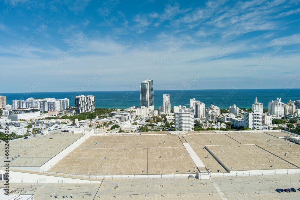 Fototapeta premium aerial shot of the Miami Beach Convention Center with blue ocean water and hotels and luxury condominiums in the city skyline, lush green palm trees, blue sky and clouds in Miami Beach Florida USA