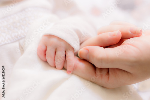 Sweet baby has her hands curled with her mother's adult hands. A closeup photo.