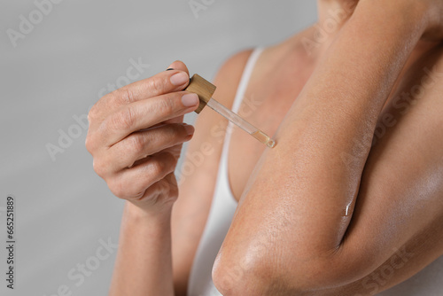 Woman applying body oil onto arm on grey background, closeup