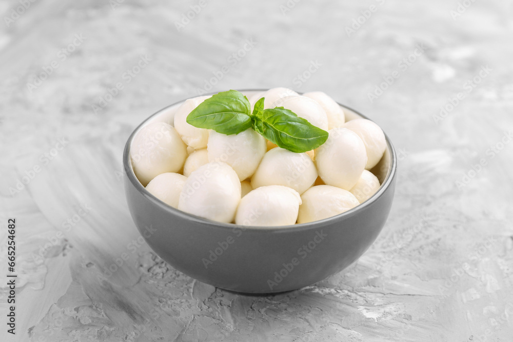 Tasty mozzarella balls and basil leaves in bowl on grey table, closeup Tasty mozzarella balls and basil leaves in bowl on grey table, closeup