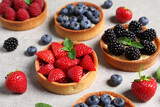 Tartlets with different fresh berries on light grey table. Delicious dessert