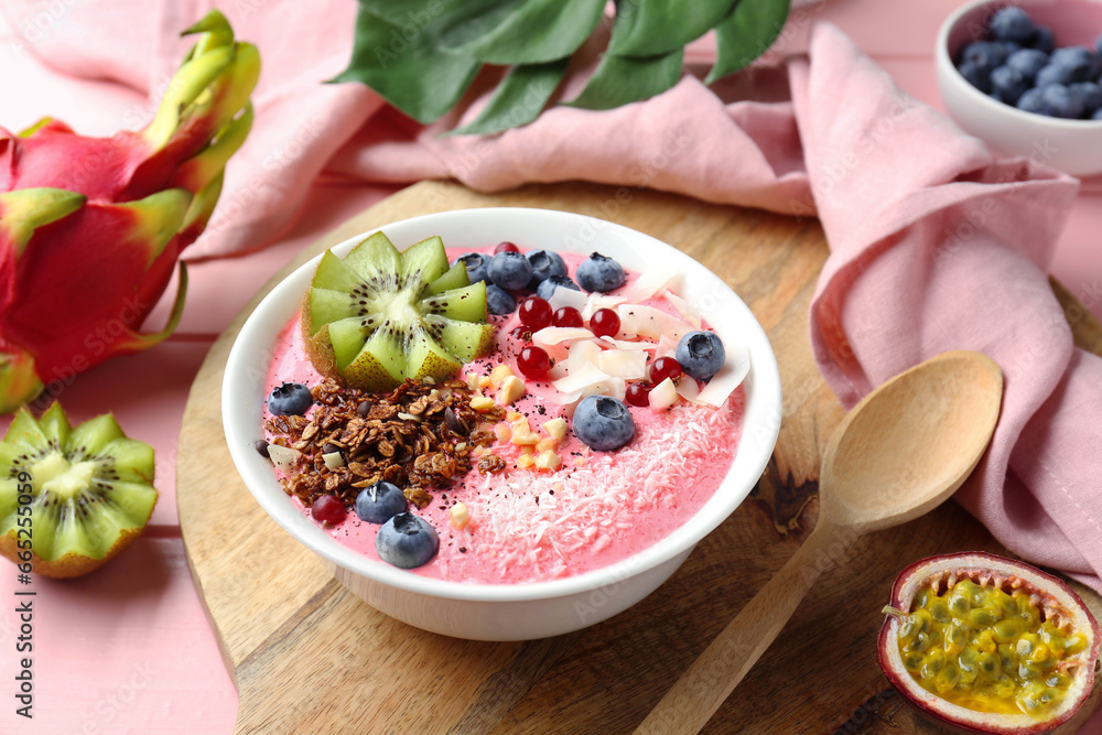 Tasty smoothie bowl with fresh kiwi fruit, berries and granola on pink wooden table