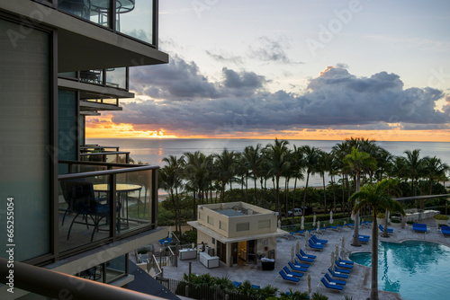 A gorgeous summer landscape with a stunning sunrise over the Atlantic ocean with powerful clouds, ocean water, balconies and lush green palm trees at Bal Harbour Beach in Miami Beach Florida USA