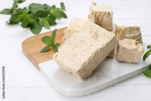 Pieces of tasty halva and mint on white wooden table, closeup. Space for text