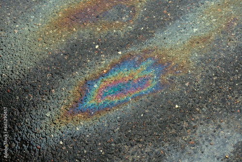 Spots of oil or gasoline are scattered randomly on the asphalt after rain. Abstract background close-up