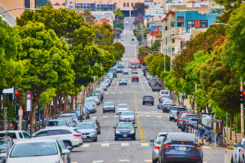 Long road ending in steep hill with traffic crisscrossing a road lined in green trees