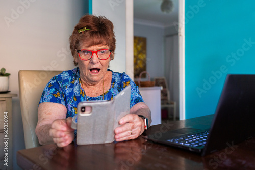 surprised older woman trying to use phone and laptop technology