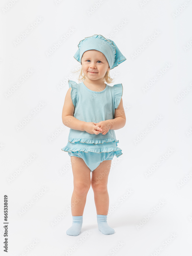A beautiful 2-year-old toddler girl stands tall, smiles and looks expressively in a summer blue dress on a white background. Photo A beautiful 2-year-old toddler girl stands tall, smiles and looks expressively in a summer blue dress on a white background. Photo