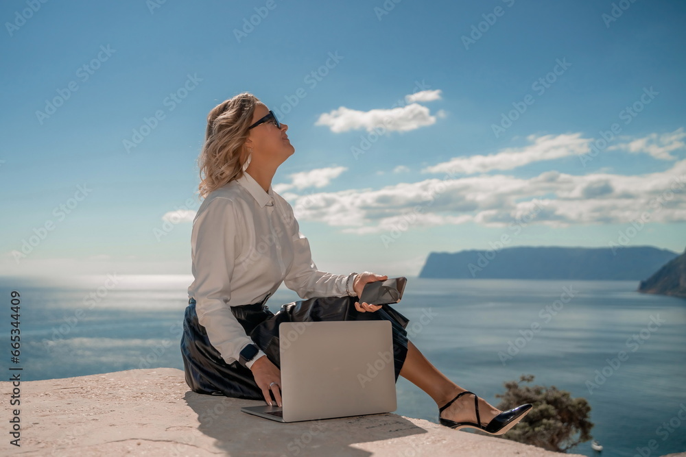 Freelance women sea working on a computer. Pretty middle aged woman with computer and phone outdoors with beautiful sea view. The concept of remote work.