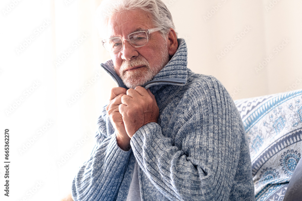 Senior man from 70s sitting at home on sofa suffering from early flu symptoms feeling cold - healthcare and people concept Senior man from 70s sitting at home on sofa suffering from early flu symptoms feeling cold - healthcare and people concept