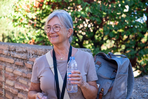 Happy senior woman visiting Granada in a sunny day listening to informations bvia audio guide holding a water bottle, Elderly woman enjoying vacation and retirement in Europe photo