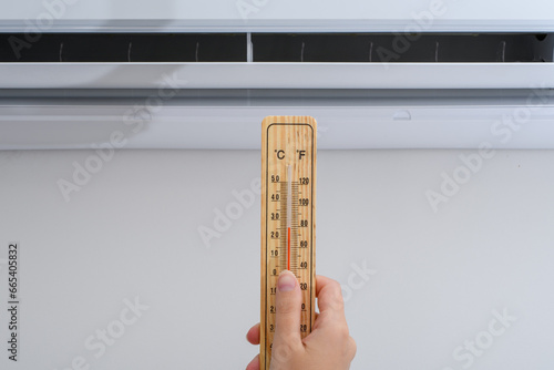 Kobieta trzyma termometr wewnętrzny na tle klimatyzatora 