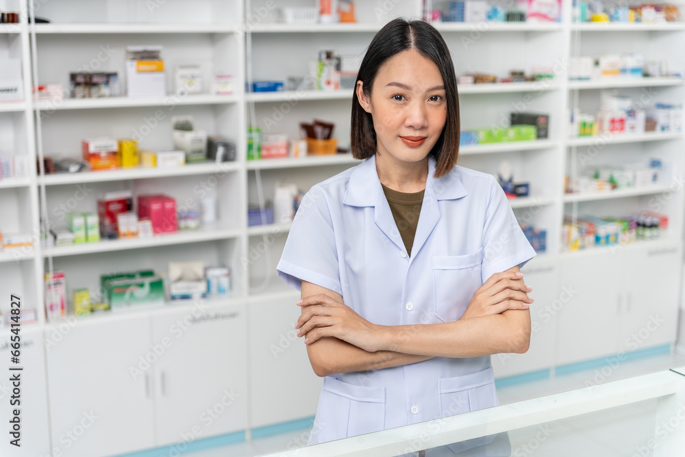 Happy beautiful asian female pharmacist wearing lab coat standing with arms crossed and looking at camera, She feels good, trustworthy and proud of his work in the pharmacy drugstore.