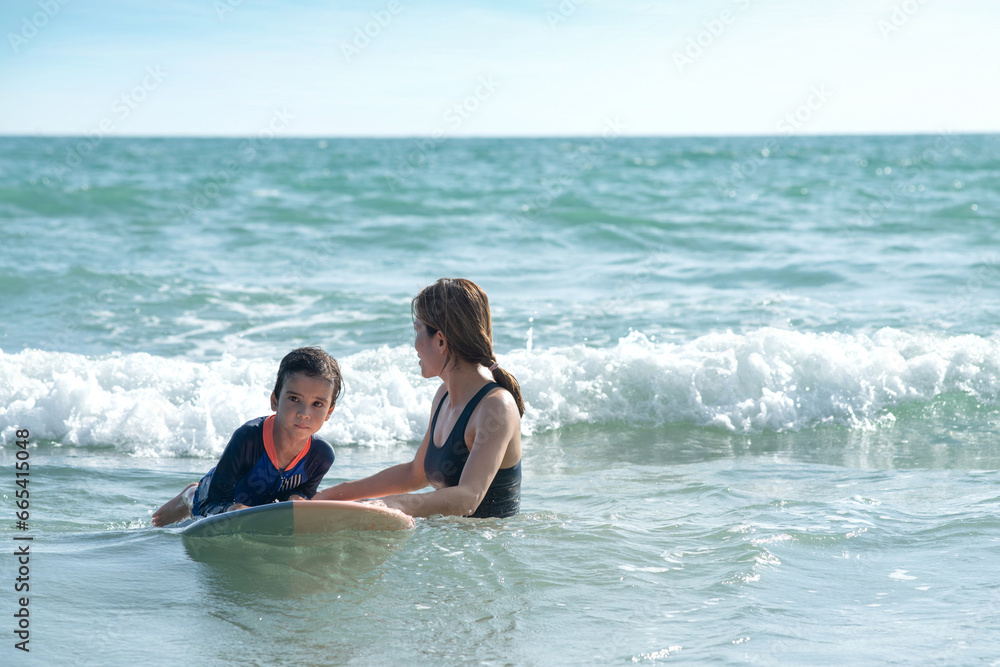 Obraz premium Little boy and mother waiting for big wave, mother teaches her son to surfing on wave, lifestyle activities, water sports