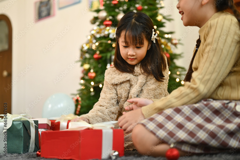 Happy little girls opening Christmas gifts while enjoying holiday season together at home Happy little girls opening Christmas gifts while enjoying holiday season together at home
