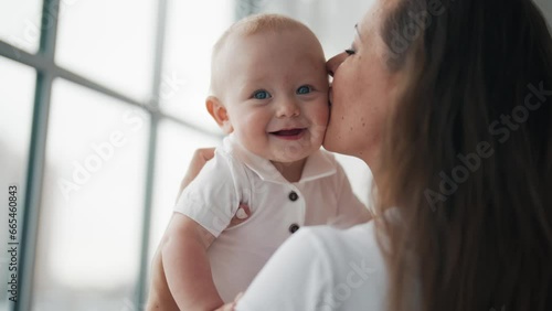 Portrait of smiling happy adorable baby standing all fours. Mom kissing little kid playing together at home. Babysitting, maternity leave motherhood babyhood parenting, mommy love and care concept.