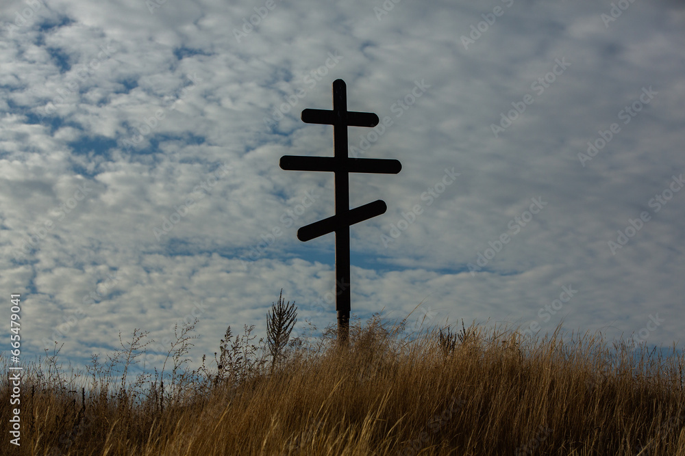 Cross on top of a hill against a blue sky with white clouds. Silhouette of a cross in the field at sunset with dramatic sky.