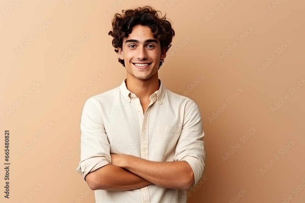 Fototapeta premium Portrait of a handsome young man with curly hair smiling at camera isolated over beige background, Happy young man. Portrait of handsome young man in casual shirt keeping arms crossed, AI Generated