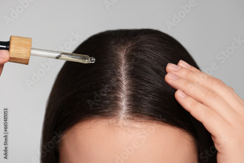 Woman applying essential oil onto hair on grey background, closeup