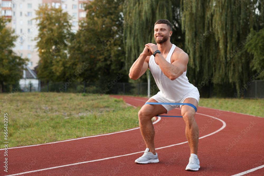 Muscular man doing exercise with elastic resistance band at stadium