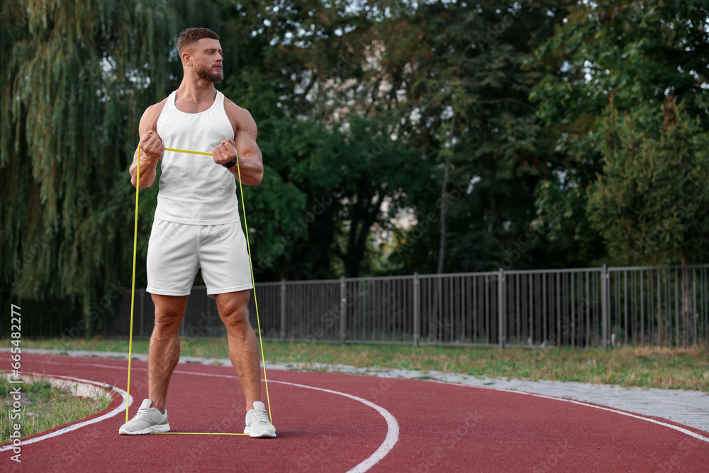 Muscular man doing exercise with elastic resistance band at stadium