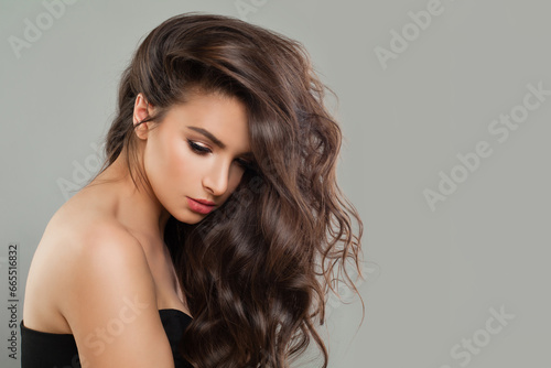 Young brunette model woman with makeup and long perfect healthy wavy brown hair posing on white background