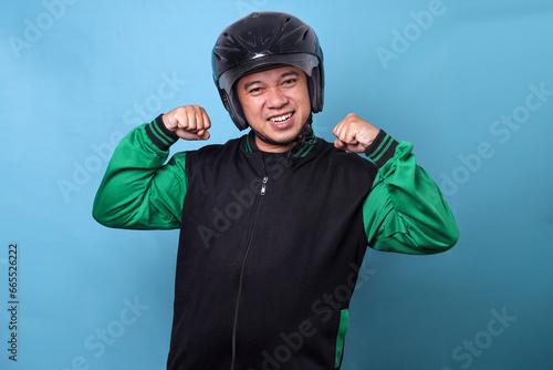 Happy online motorcycle taxi driver wearing helmet raising arms over blue background