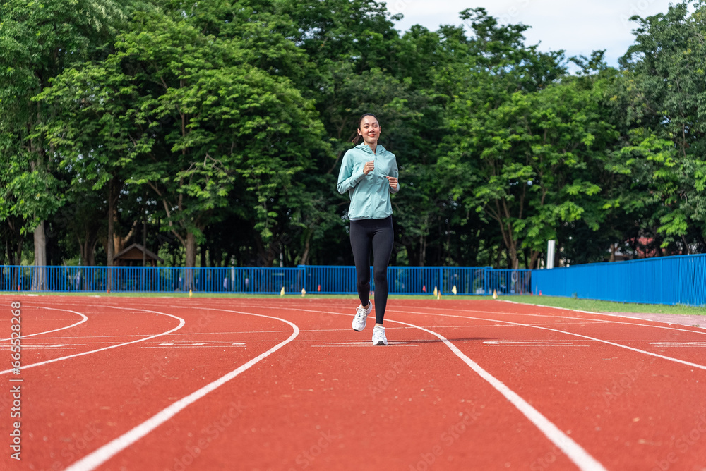 Young Asian women are exercising with outdoor running with a running track background in the morning. Concept healthy running and outdoor exercise,Tracking shot, Young Asian women are exercising with outdoor running with a running track background in the morning. Concept healthy running and outdoor exercise,Tracking shot,