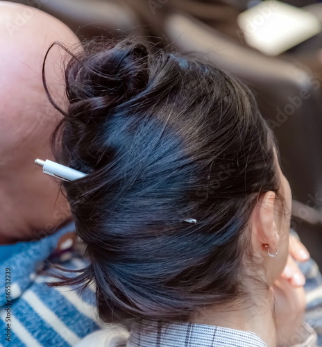Ballpoint pen pinned into the hair of a woman 's hairstyle close - up