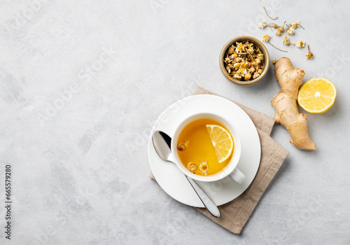 Chamomile herbal tea with lemon in a white cup on a light background with dry flowers and ginger. The concept of a healthy detox drink for health and immunity.
