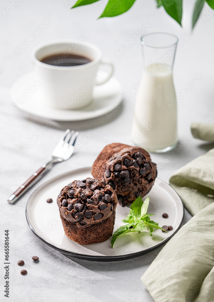Chocolate muffins on a white plate with mint on a light background with cup of coffee, milk and branch. Chocolate muffins on a white plate with mint on a light background with cup of coffee, milk and branch.