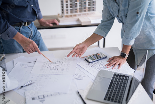 Two engineer architect pointing on blueprint of sketching interior architectural building to discussion technical for construction plan and building model while working together in workplace site