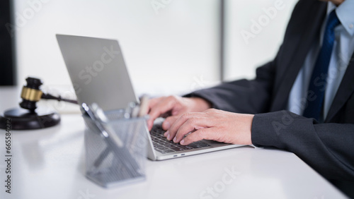 Male lawyer typing data and reading financial document of business on laptop to analysis about legal agreement and terms of business contract while working on the desk with hammer in law firm