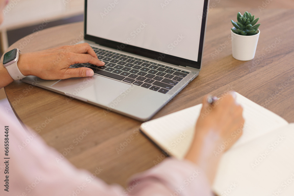 Female entrepreneur working at home to searching business data on laptop and writing notes in paper Female entrepreneur working at home to searching business data on laptop and writing notes in paper
