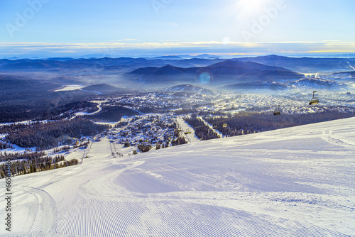 View from mount Green of slopes in Sheregesh ski resort, Sheregesh village, picturesque panoramic landscape with range mountains and hills, forest, blue sky, sun and snow, sunny winter weather
