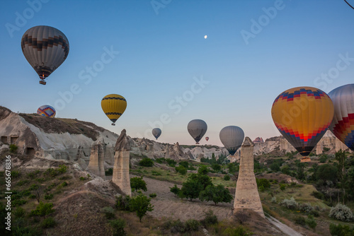Hot air balloons flying over bizarre rock landscape in Cappadocia. Balloons fly early in the morning. Beautiful hot air balloons in the morning sky. Moon in the sky. Goreme. Turkey
