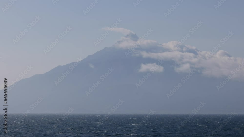 Sailing calm sea by clouds swept over volcanic island peak on sunny day Sailing calm sea by clouds swept over volcanic island peak on sunny day
