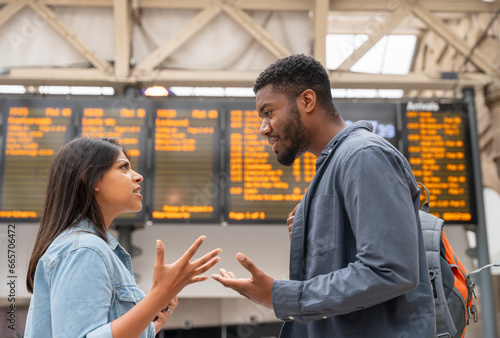 Young couple arguing in front of timetable at a railway station as they missed the train