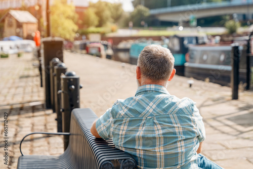 Fotografia Back of a mature man sitting on a bench at a quay enjoing last warm days of the