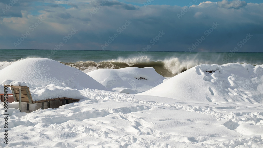 Snow covered coast and bench with stormy sea background Snow covered coast and bench with stormy sea background