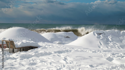 Snow covered coast and bench with stormy sea background © Luka