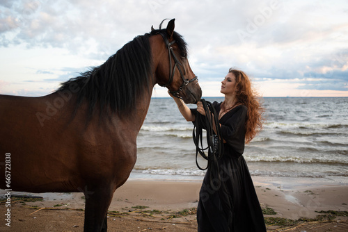 beautiful young rider in a dress and with her hair down, leads her horse along the beach. horseback riding in the open air