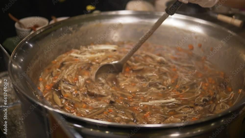 A woman in Bangkok is cooking food in a traditional Thai pot, while stirring it A woman in Bangkok is cooking food in a traditional Thai pot, while stirring it