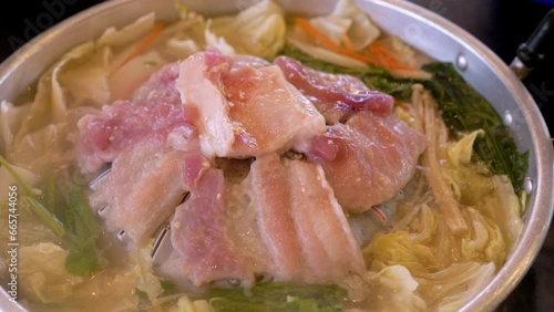 Steaming hot pot filled with thinly sliced meat and loads of vegetables, cooked on a stove top using induction heat. photo