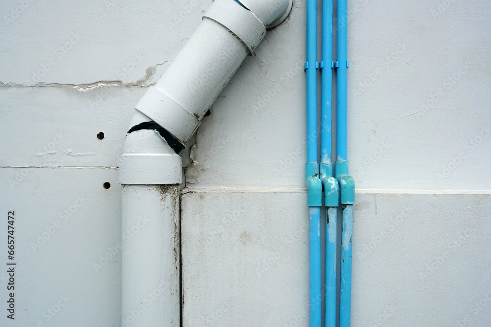 Close up a white broken plastic pipe with small blue plastic pipe on the wall of the building