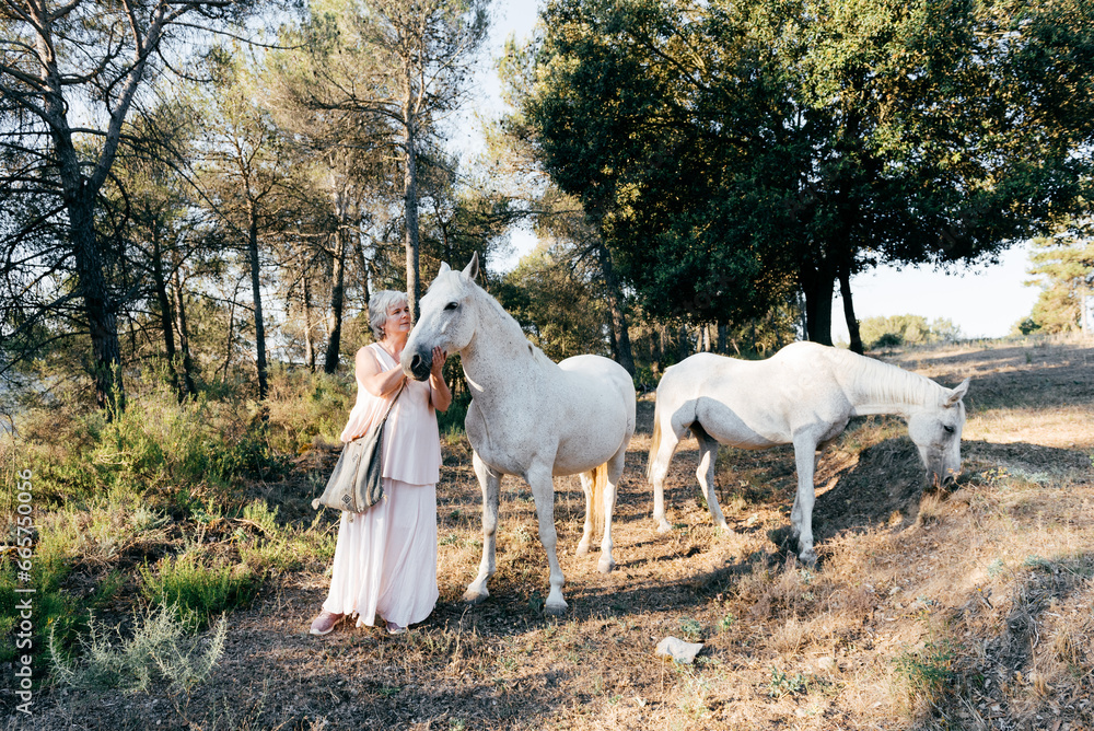 Middle aged woman standing near gray horse in daylight Middle aged woman standing near gray horse in daylight